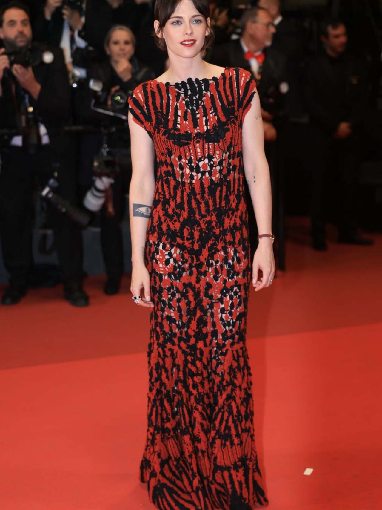 At Cannes 2026, Kristen Stewart wore a rebellious, semi-sheer red and black Chanel gown designed by Matthieu Blazy for the Full Phil premiere. The graphic, body-skimming maxi dress was intricately crafted from heavily textured beaded mesh and crochet leaves, creating a shredded, naked-illusion pattern. Defying the strict festival dress code, stylist Tara Swennen paired the look with black Converse high-top sneakers hidden beneath the fringed hem. A bold red lip, a new pixie cut with curtain bangs, and Chanel High Jewelry completed the effortless look At Cannes 2026, Kristen Stewart wore a rebellious, semi-sheer red and black Chanel gown designed by Matthieu Blazy for the Full Phil premiere. The graphic, body-skimming maxi dress was intricately crafted from heavily textured beaded mesh and crochet leaves, creating a shredded, naked-illusion pattern. Defying the strict festival dress code, stylist Tara Swennen paired the look with black Converse high-top sneakers hidden beneath the fringed hem. A bold red lip, a new pixie cut with curtain bangs, and Chanel High Jewelry completed the effortless look