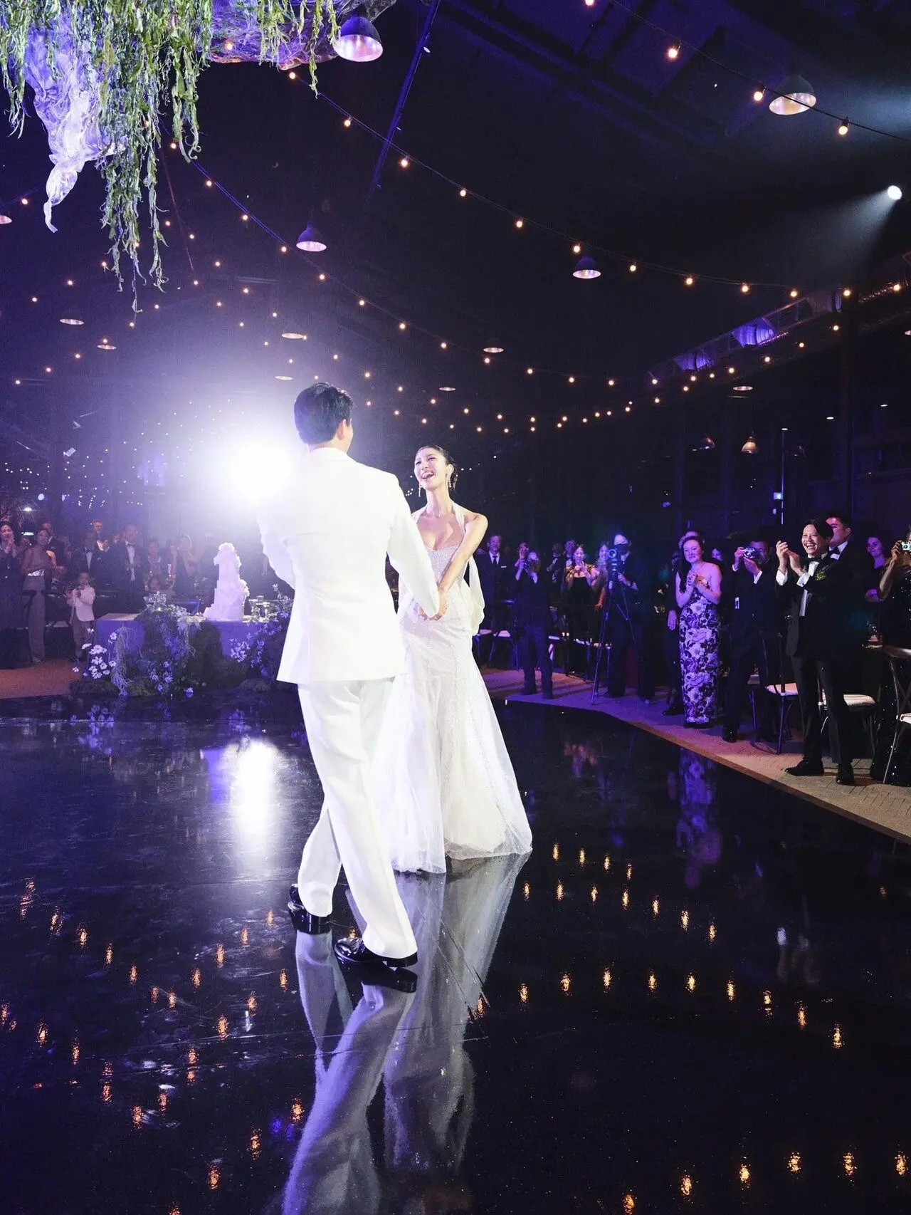 EJAE and Samuel Kim celebrated their wedding with a romantic first dance inside a glass-house venue in Seoul. Warm string lights and a glossy black floor set the mood