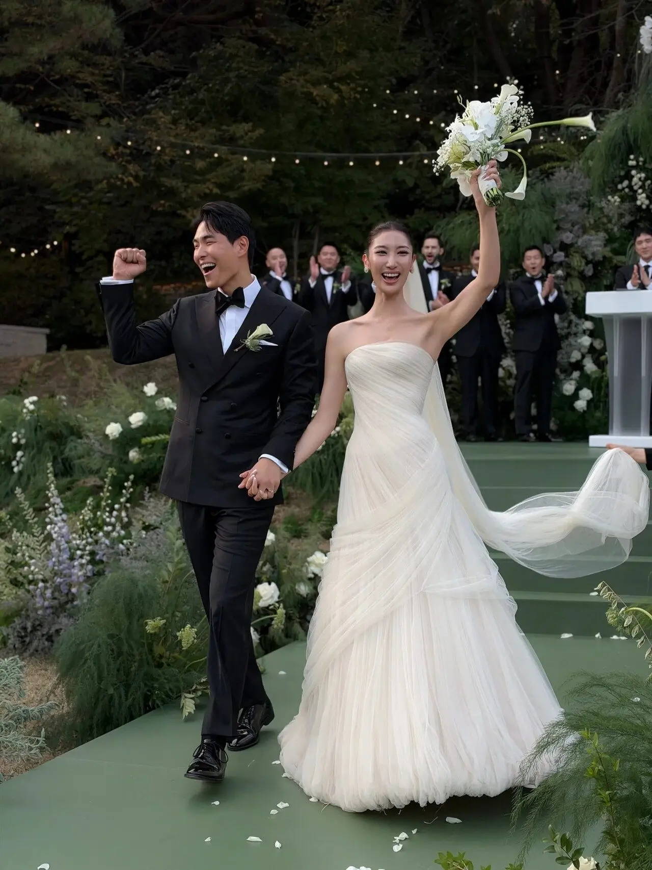 EJAE raised her bouquet as Samuel Kim pumped his fist in celebration after their vows. Their wedding party applauded as the newlyweds walked down the aisle together