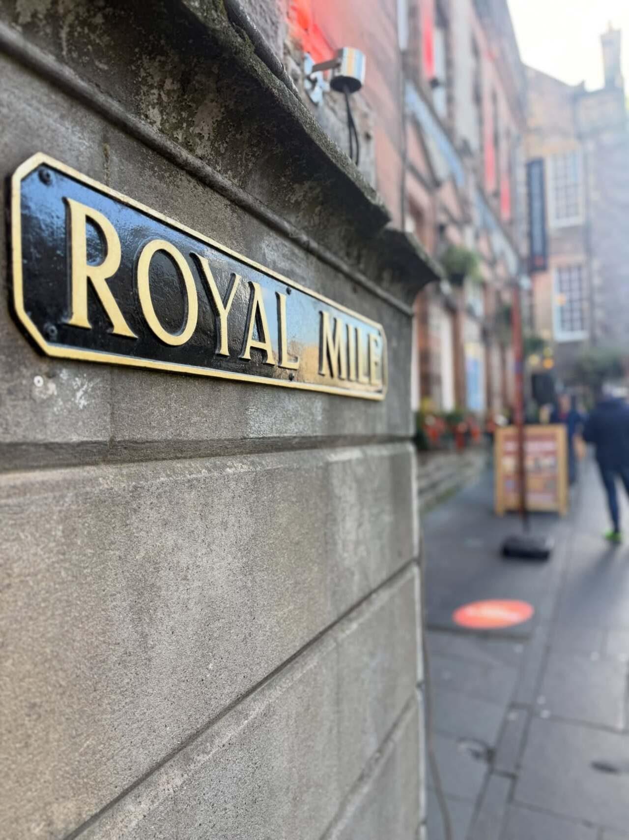 A classic black-and-gold Royal Mile sign marks one of Edinburgh’s most recognisable streets, with the historic thoroughfare stretching into the background