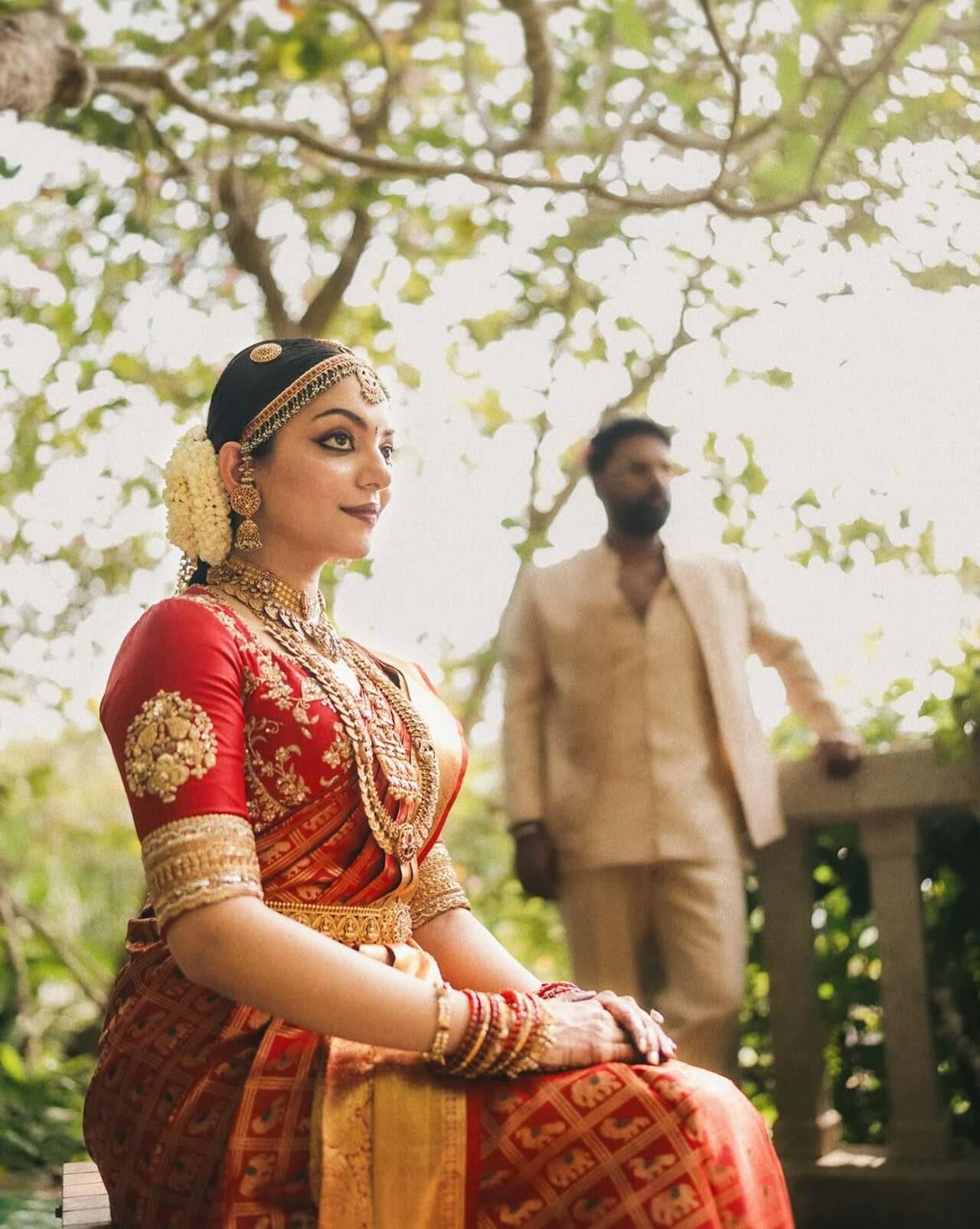 Ahaana sits gracefully in the foreground. The picture focuses on her temple jewelry, and jasmine-adorned hair braid, while Nimish stands slightly out of focus in the background, giving a cinematic shot