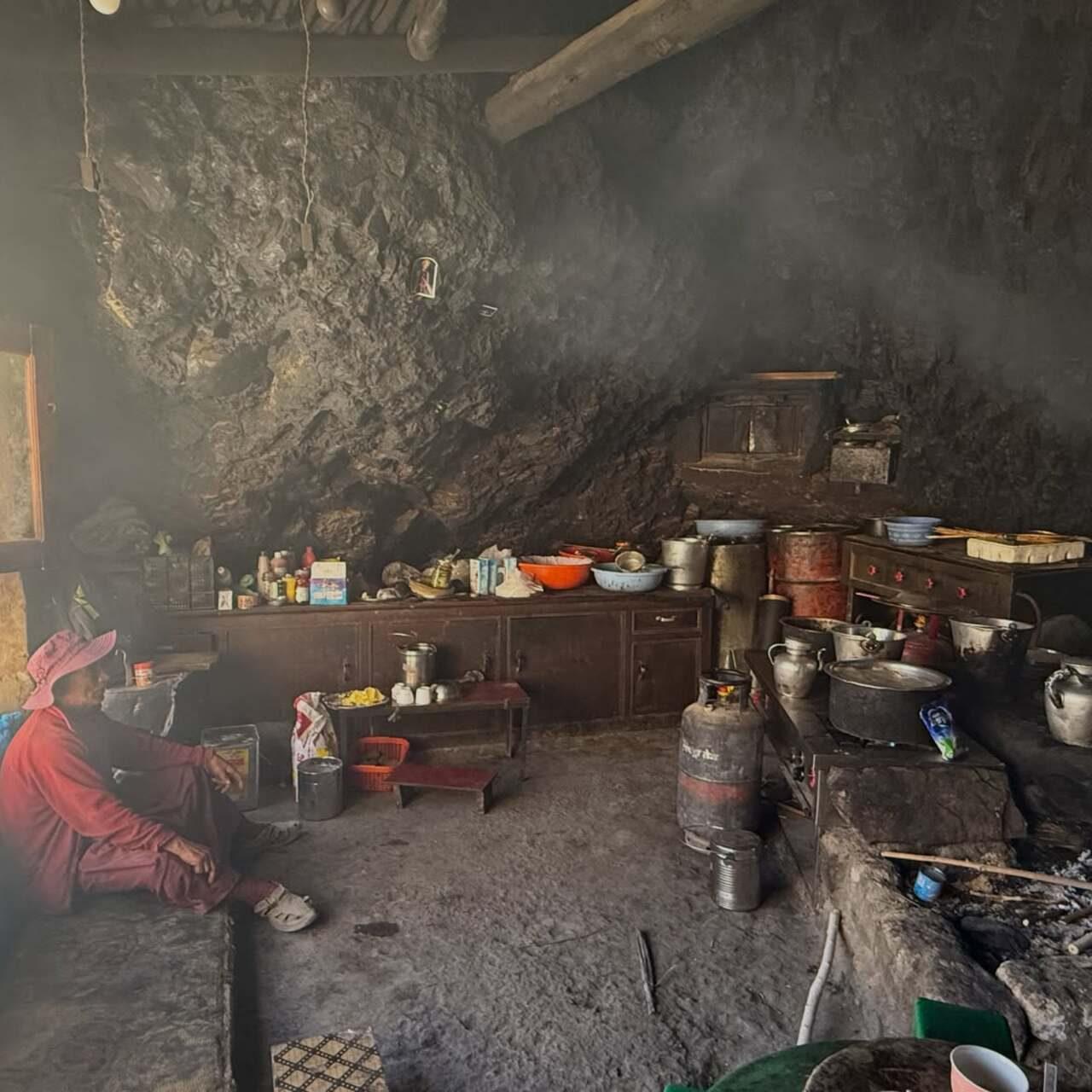 Another interior shot offers a glimpse into local life inside a cozy, cavernous mountain kitchen carved right into rock walls, complete with traditional cookware, gas cylinders, and a local resident seated inside. Another interior shot offers a glimpse into local life inside a cozy, cavernous mountain kitchen carved right into rock walls, complete with traditional cookware, gas cylinders, and a local resident seated inside.