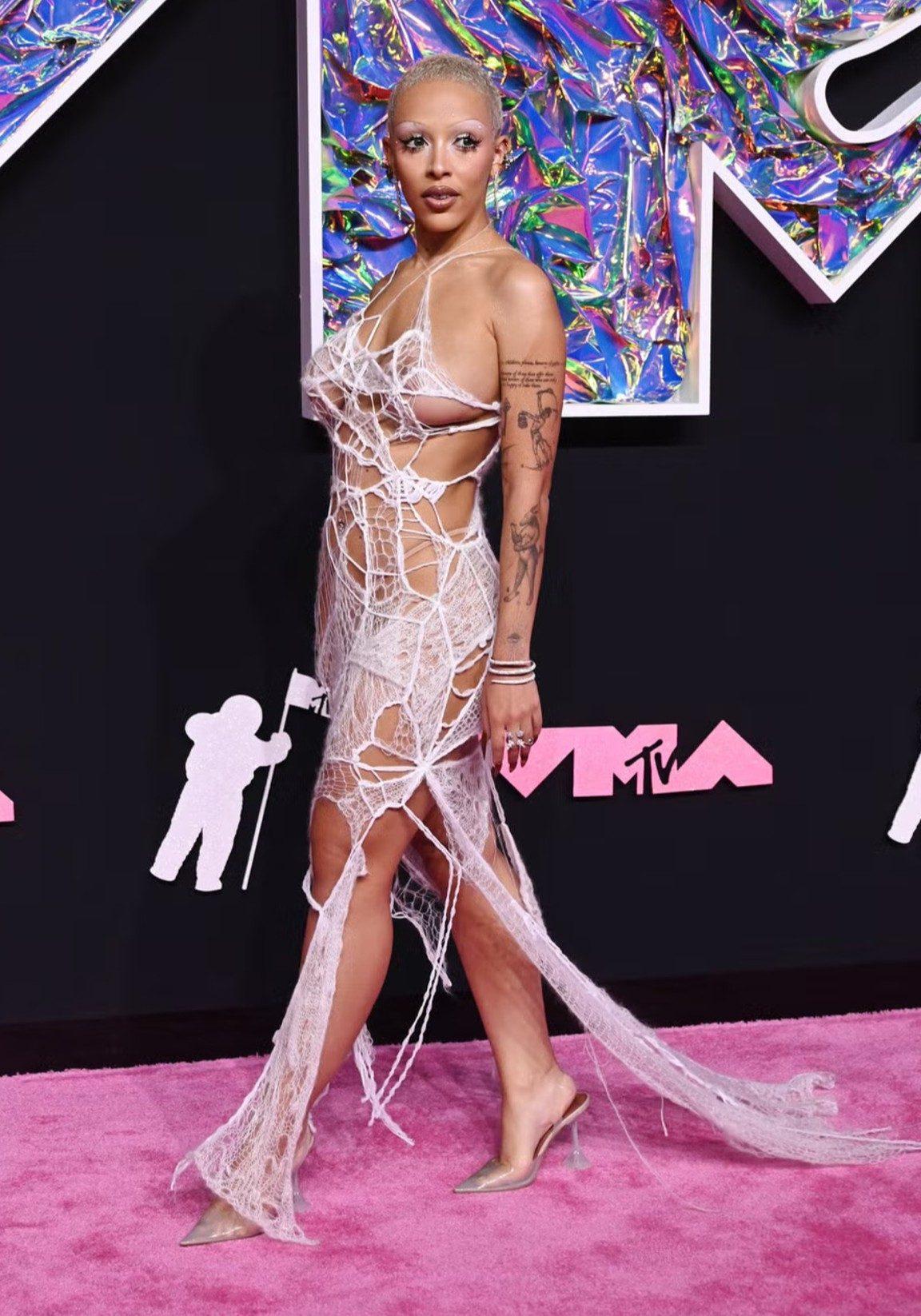At the 2023 MTV Video Music Awards, Doja Cat made a statement in a daring spiderweb-inspired gown by Turkish designer Monse. The sheer off-white look featured intricate web-like cutouts, which she paired with a shaved blonde hairstyle and bleached brows. At the 2023 MTV Video Music Awards, Doja Cat made a statement in a daring spiderweb-inspired gown by Turkish designer Monse. The sheer off-white look featured intricate web-like cutouts, which she paired with a shaved blonde hairstyle and bleached brows.