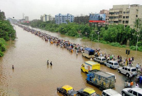 In pic: Commuters walk through flooded streets after torrential rains paralysed Mumbai on July 26, 2005.