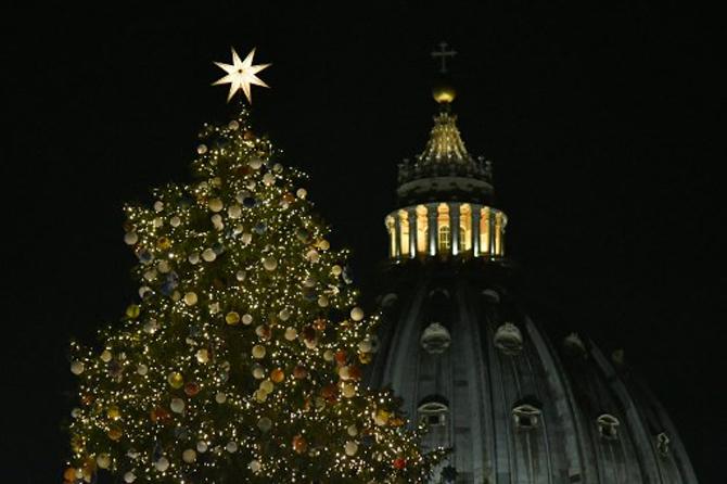 The Christmas tree of St Peter's square is illuminated with the dome of St Peter's Basilica in the background during the inauguration of the Christmas crib in Vatican
