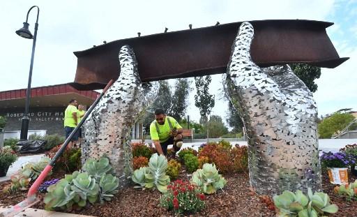 Abraham Galindo cleans the area around artist Heath Satow's sculpture honoring victims of the 9/11 World Trade Center attacks, on September 11, 2017, in Rosemead, California. The sculpture contains 2,976 stainless-steel doves, representing victims of the 2001 attacks, welded together to create a pair of giant hands lifting an original piece twisted steel beam from New York's World Trade Center.