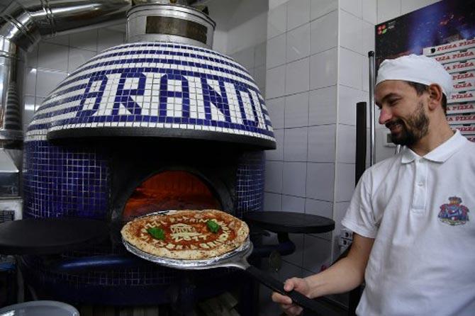 In this photo, a Neapolitan pizza maker poses next to the oven with a pizza celebrating the UNESCO decision to make the art of Neapolitan 'Pizzaiuolo' an 'intangible heritage'