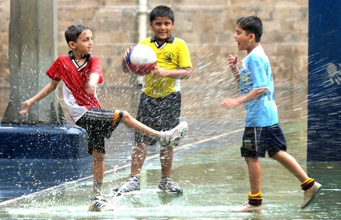 School children play in a puddle after a rain shower in Mumbai on July 18, 2013