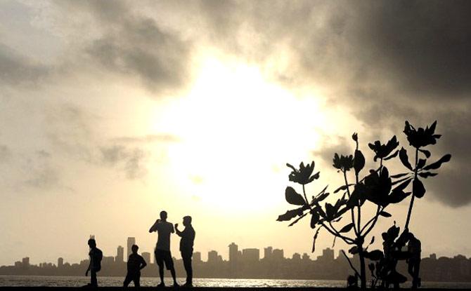 People stroll near the seafront as dark clouds gather over city skyline in Mumbai on June 27, 2012