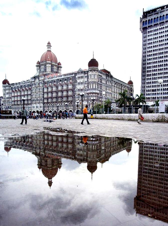 A pool of rainwater following a monsoon rain shower reflects an image of the Taj Mahal hotel as people pass by in Mumbai on September 26, 2003