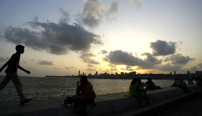 Sightseers enjoy the last rays of light as the sun sets behind pre-monsoon clouds hovering over The Arabian Sea in Mumbai on May 12, 2007