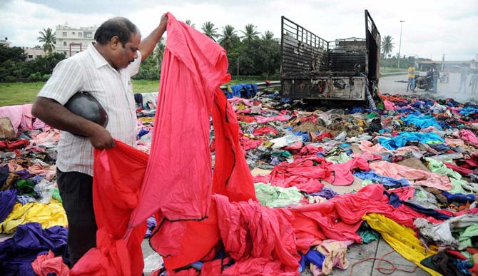 A man collects valuable remains from a Tamil Nadu Goods truck that was set on fire by the protesters during protests over Cauvery issue, at Nice Road in Bengaluru on Tuesday. Pic/PTI 