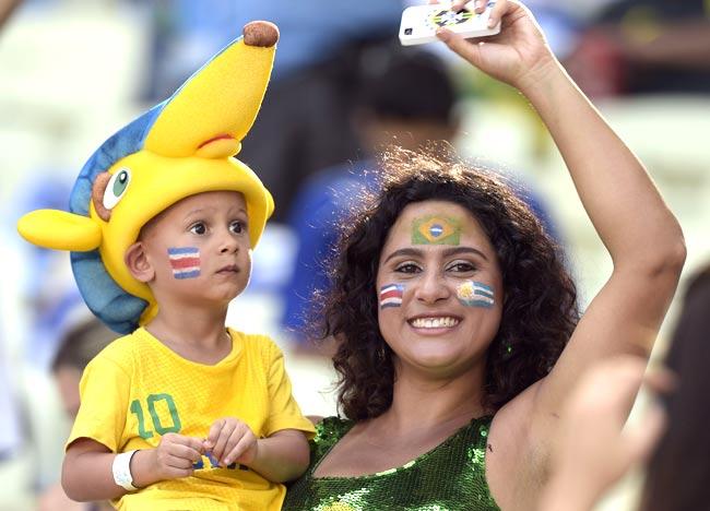 A football fan with a child is made up in the colors of Brazil (top), Uruguay (R) and Costa Rica (L) prior to a Group D football match between Uruguay and Costa Rica