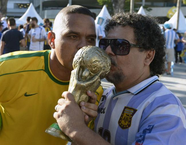 Two men depicting former football stars Ronaldo (L) of Brazil and Diego Maradona of Argentina kiss a mock-up World Cup trophy outside the Maracana stadium