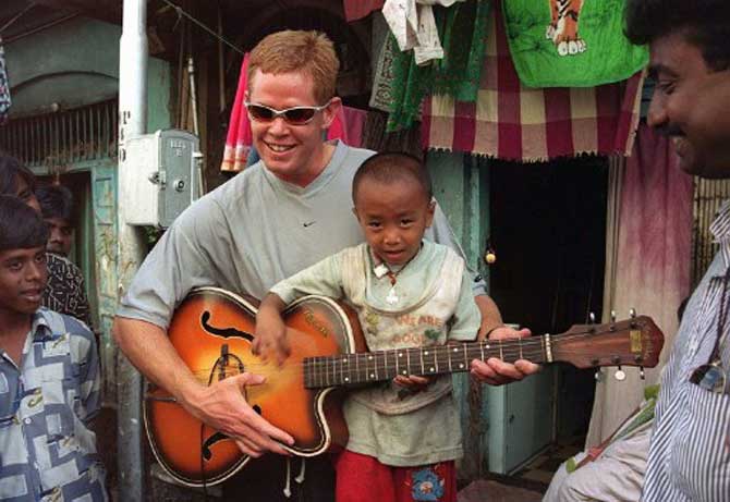 South African cricketer Shaun Pollock plays the guitar with a child of a sex worker in February 2000 during a visit to Bombay's notorious Kamatipura red-light district.